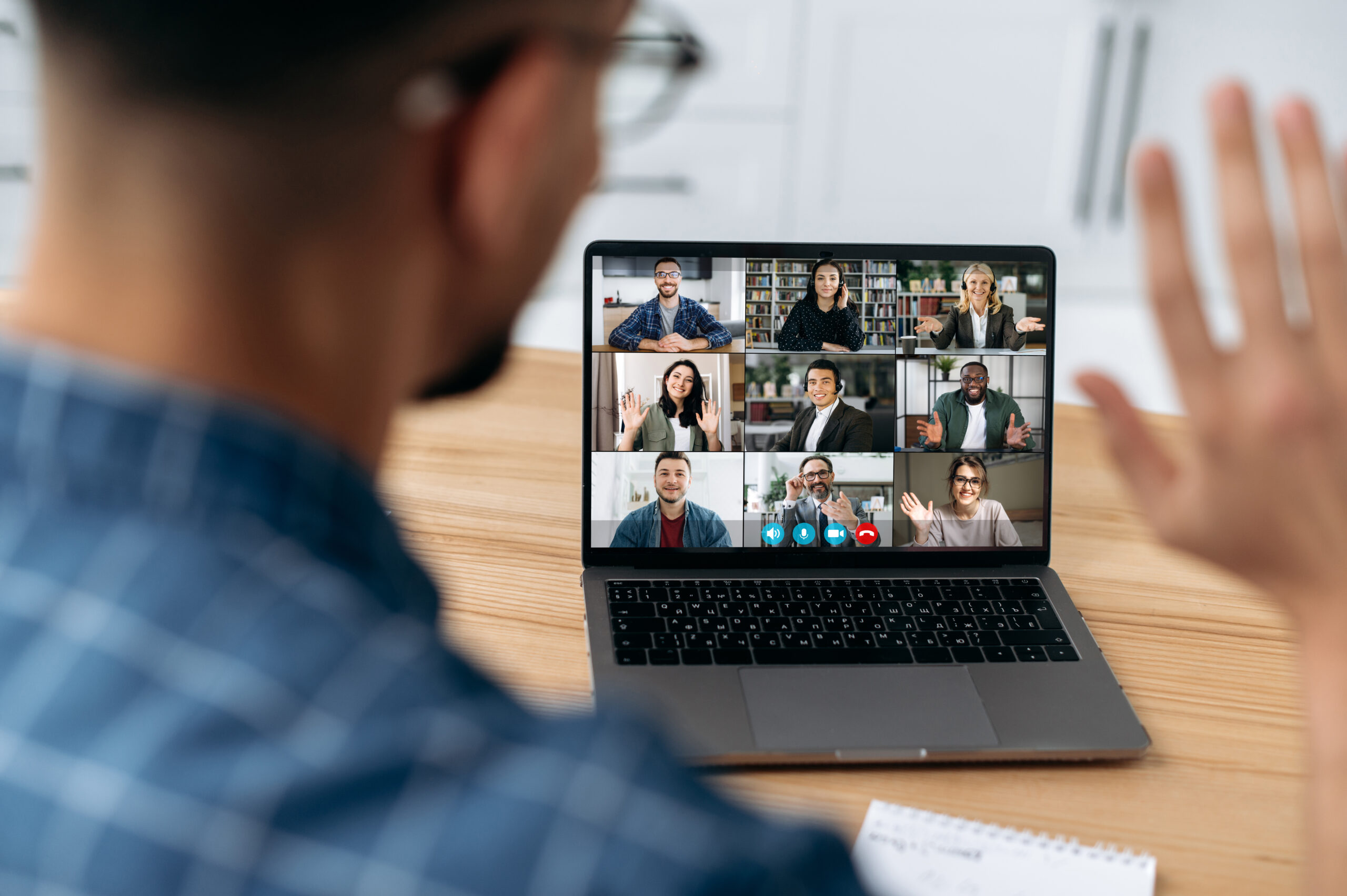 Online video communication concept. Over shoulder view at a laptop screen with different people, employees, business partners, guy greets colleagues, online briefing, brainstorming, group conversation